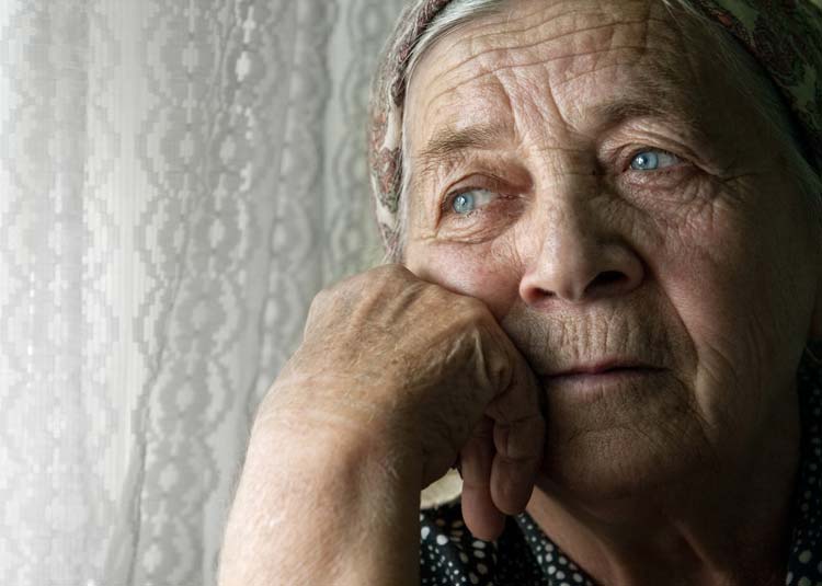 Ältere Frau schaut traurig aus Fenster