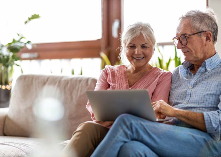 Älteres Paar sitzt gemeinsam auf Sofa mit Laptop