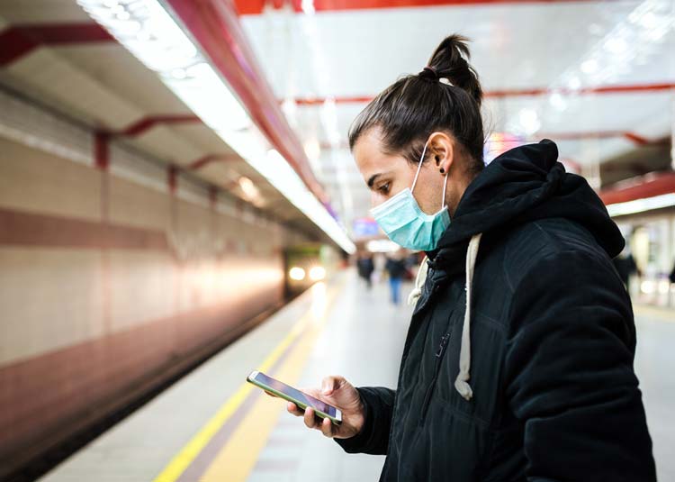 Mann mit Mundschutz steht an U-Bahn-Station und schaut auf Mobiltelefon © miladrumeva - stock.adobe.com Mann mit Mundschutz steht an U-Bahn-Station und schaut auf Mobiltelefon